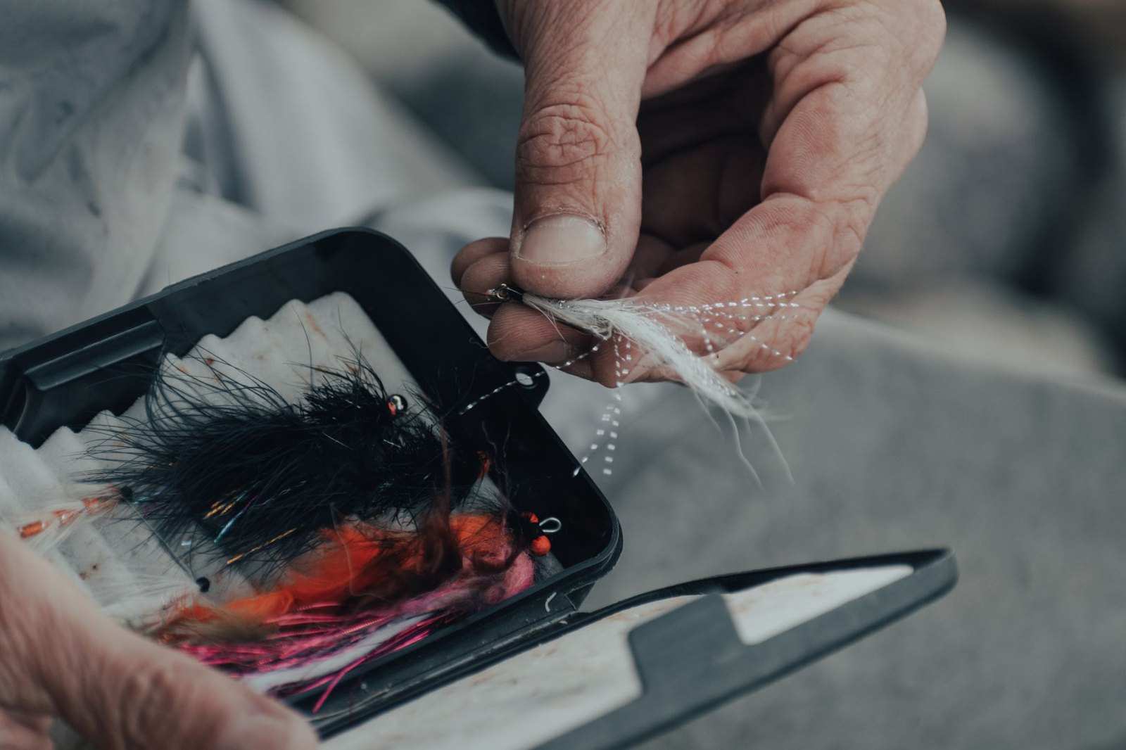 A hand selecting a fly from an open fly box