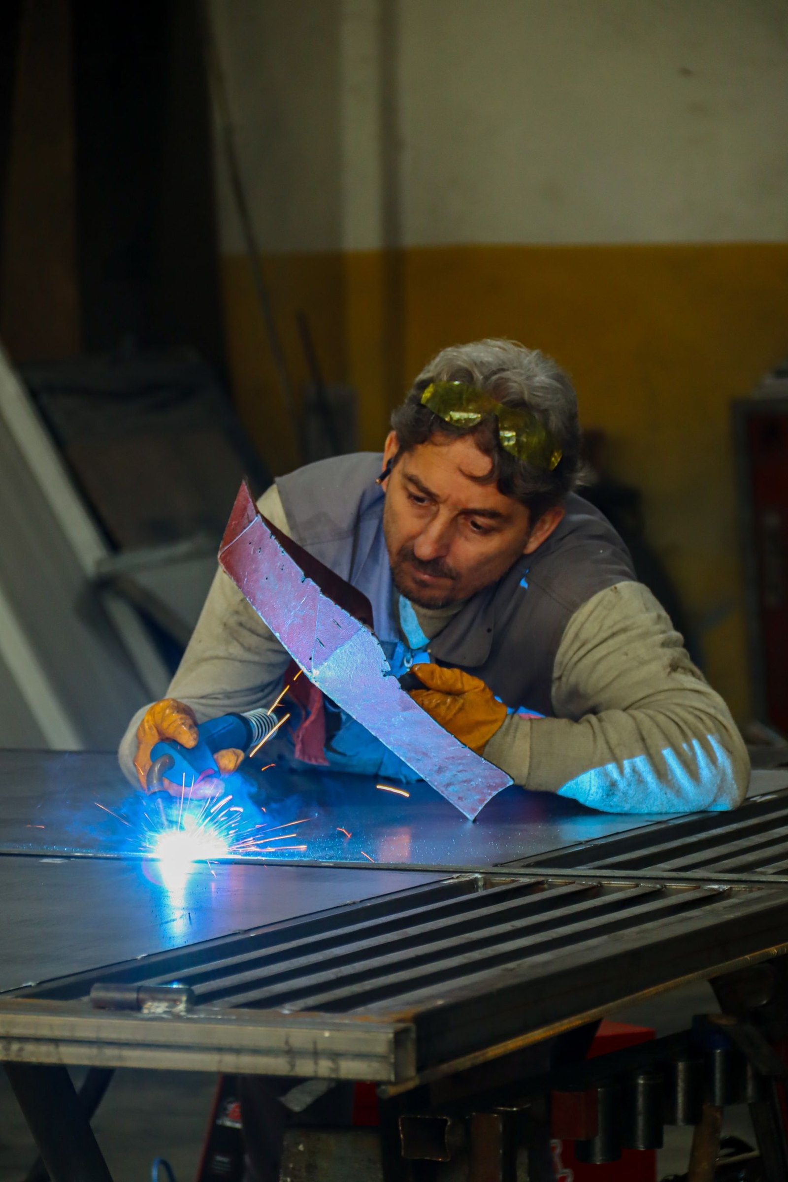 A welder working on a steel piece at a bench with sparks